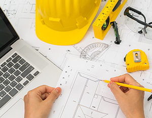 Hand over Construction plans with yellow helmet and drawing tools on blueprints